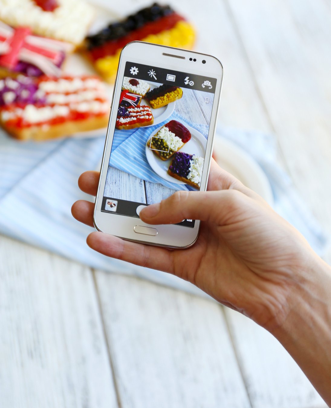 Hand Making Photo of Sandwiches with Flags on Mobile Phone for Social Network